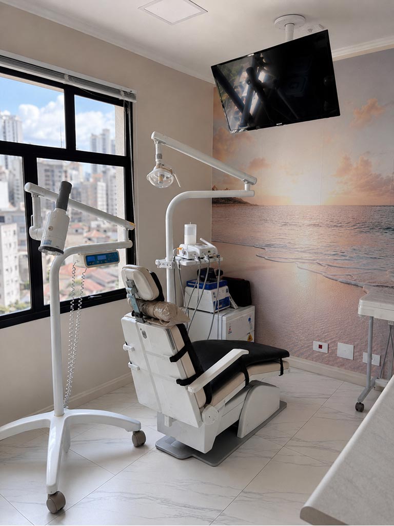 Sala de atendimento da Dra. Daiane Carvalho, com cadeira odontológica, foco cirúrgico e janela com vista da cidade
