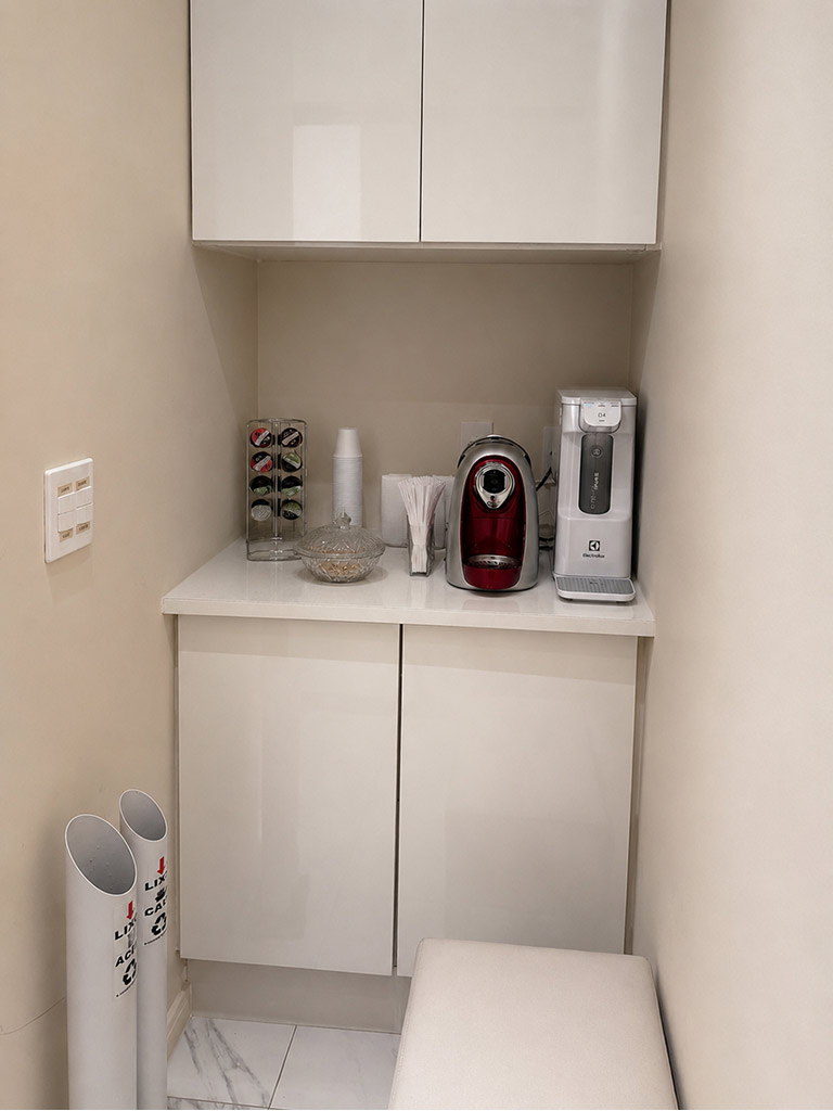 Espaço de cortesia do consultório, com máquina de café e purificador de água à disposição dos pacientes
